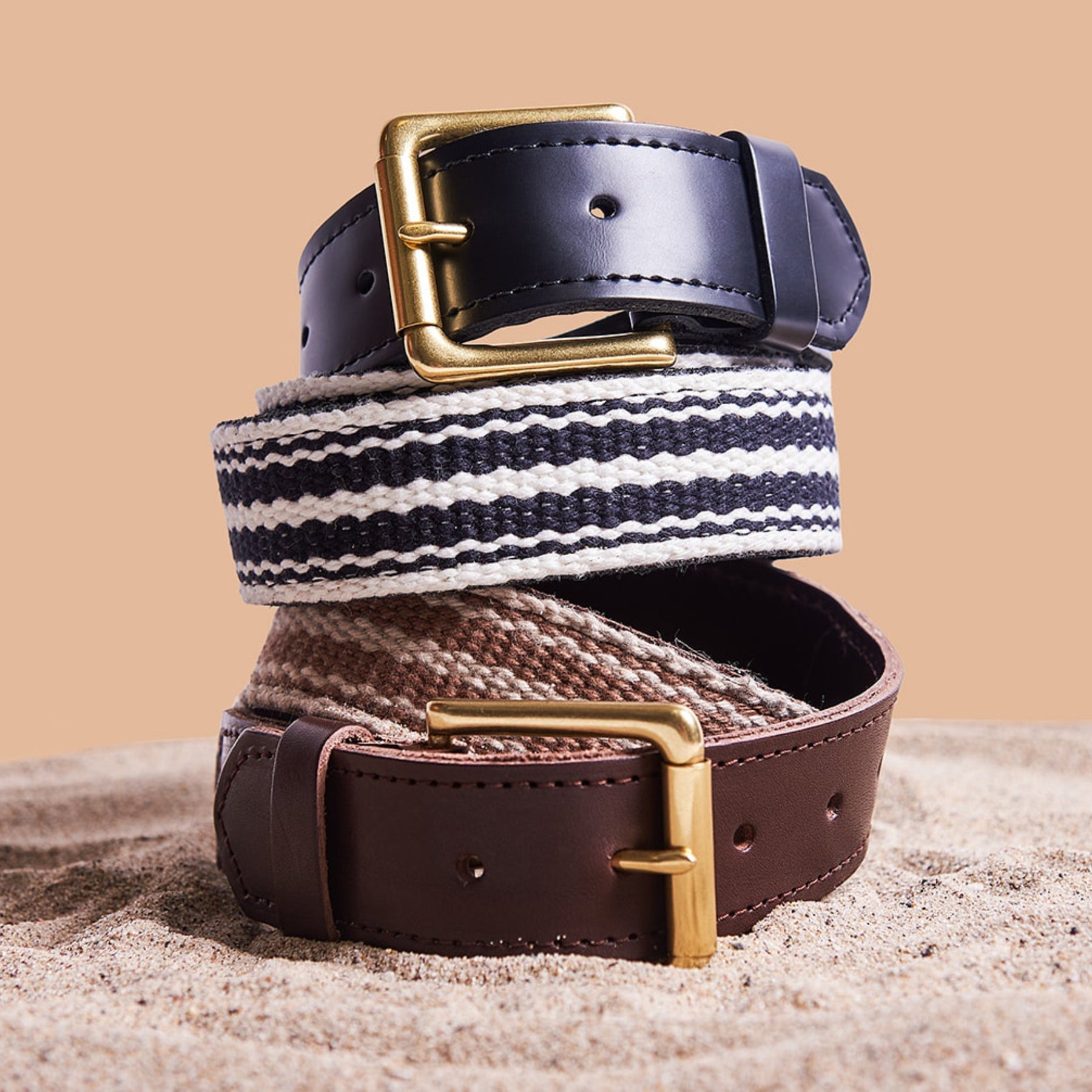 Two belts with striped patterns and gold buckles on a beige background