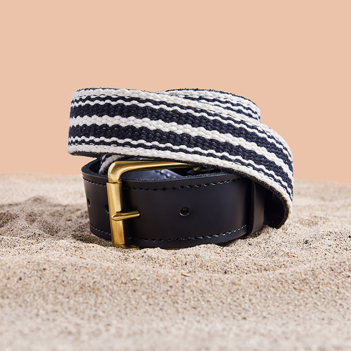 Striped woven belt with a gold buckle on sand
