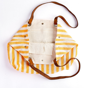 A striped canvas shoulder bag with yellow and white vertical stripes, brown leather straps, and silver metal hardware, shown on a plain white background.